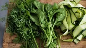 Fanes de carotte et de radis à côté d'épluchures de courgette sur une planche
