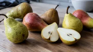Poires entières de variétés différentes sur un plan de travail en bois, dont une coupée en deux